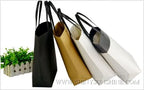 Black, gold, white, and silver tote bags on a white background with a plant in the corner.