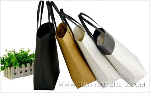 Black, gold, white, and silver tote bags on a white background with a plant in the corner.